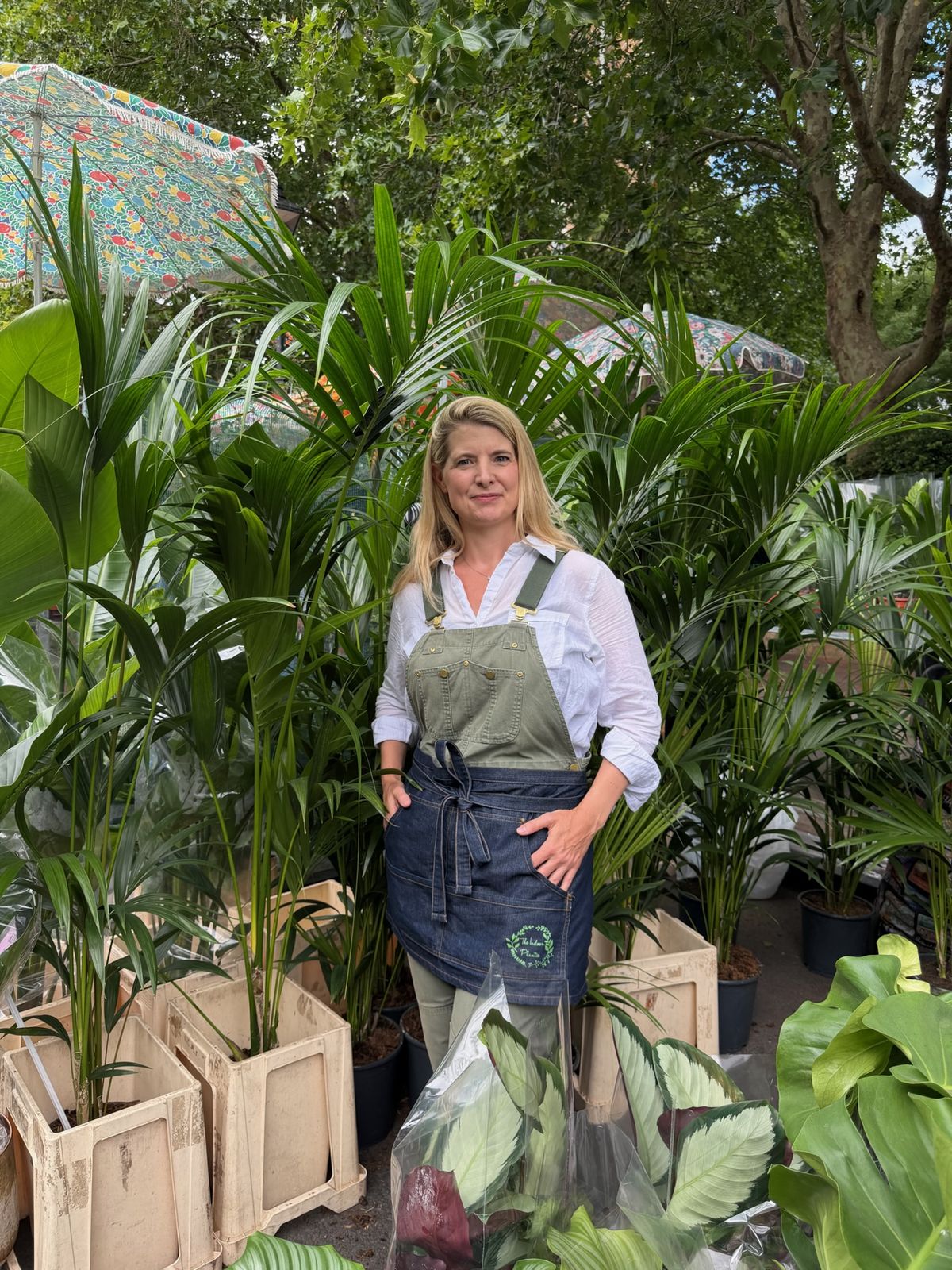 Alexa of The Indoor Plantie in her branded apron among kentia palms at a London plant market